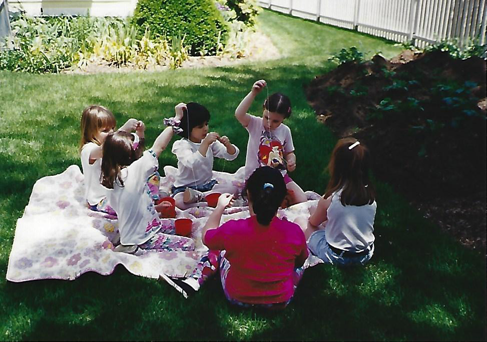 A group of young girls sitting on a blanket and making jewelry at Christy's fifth birthday party